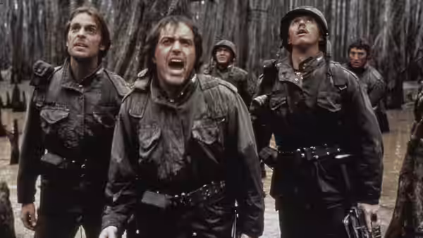 Soldiers in muddy uniforms stand in a flooded forest