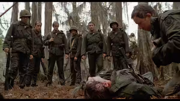 Soldiers gather around a body lying on the forest floor