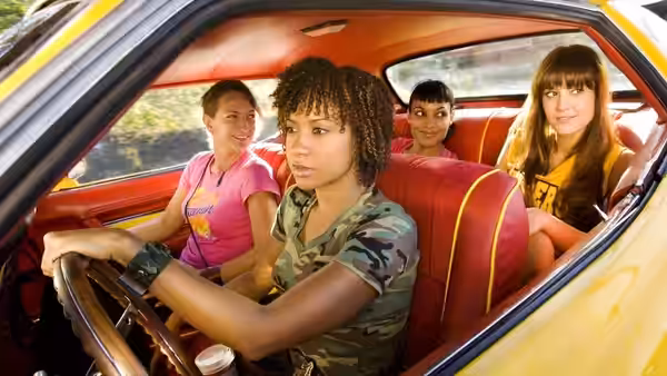 Four women seated inside a yellow car with red upholstery, driver at the wheel