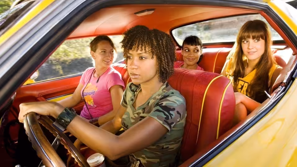 Four women seated inside a yellow car with red upholstery, driver at the wheel