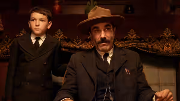 Daniel Plainview (Daniel Day-Lewis) and H.W. Plainview (Dillon Freasier) seated indoors in suits
