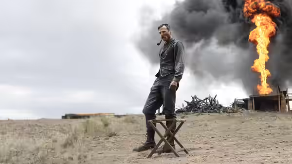 Daniel Plainview (Daniel Day-Lewis) stands by stool with huge fire behind him