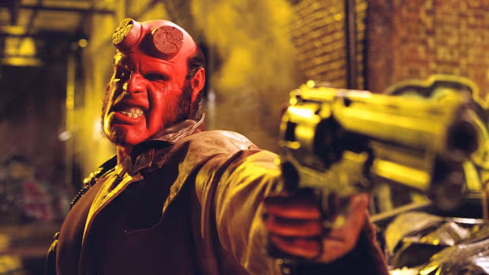 Hellboy (Ron Perlman) aiming a large golden revolver forward in an alley