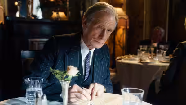 Williams (Bill Nighy) writes at a restaurant table set with water glasses and flowers
