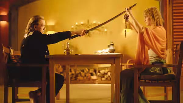 Bill (David Carradine) and Beatrix Kiddo (Uma Thurman) crossing swords at a table