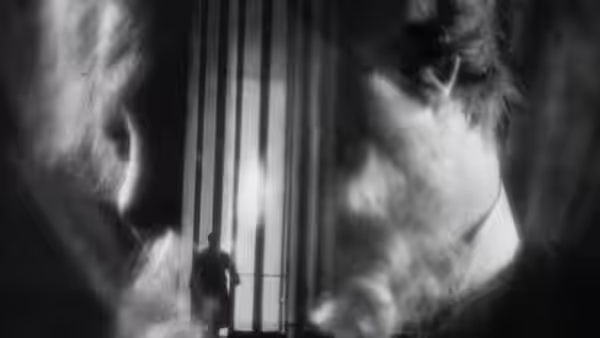 A small figure stands between tall illuminated windows, framed by blurred shadows