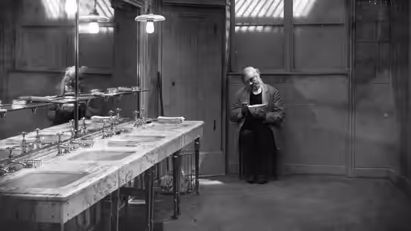 Hotel doorman Emil Jannings stands alone in a washroom, holding a paper