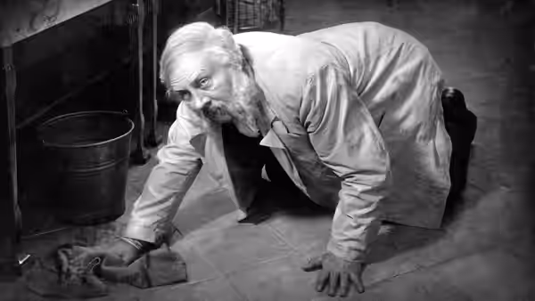 Hotel doorman Emil Jannings crawls across a tiled room toward clothing on the floor