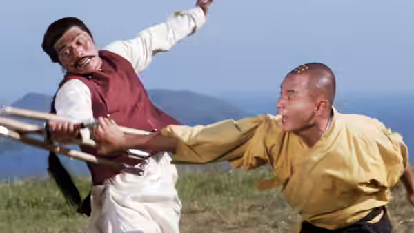 Liu Yu-de (Gordon Liu) grapples with an opponent's staff in a grassy field