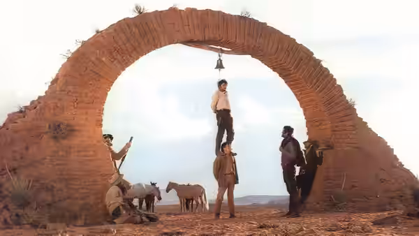 A man stands on another's shoulders to reach a bell under a brick arch