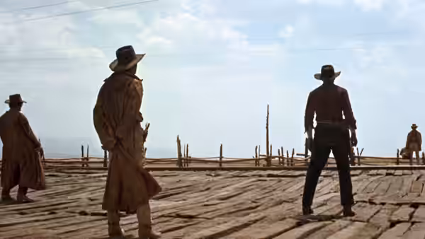 Four men in hats and dusters stand on a wooden platform in open country