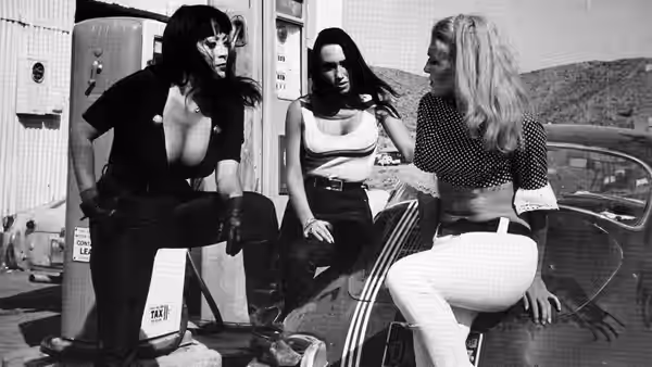 Three women gather beside a car at a gas station