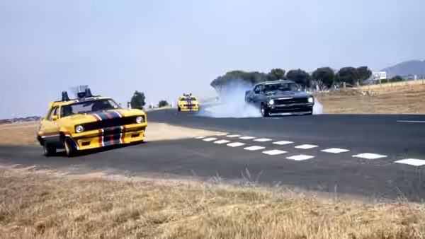 Yellow police car chasing a black vehicle on a rural road with tire smoke