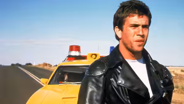 Max Rockatansky (Mel Gibson) standing beside a yellow police car on a road