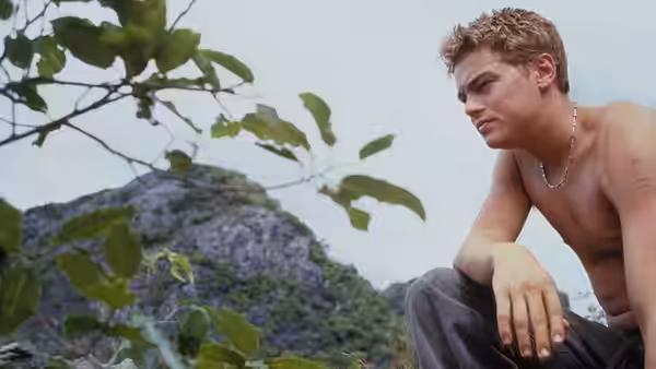 Richard (Leonardo DiCaprio) sitting shirtless outdoors with mountains behind him
