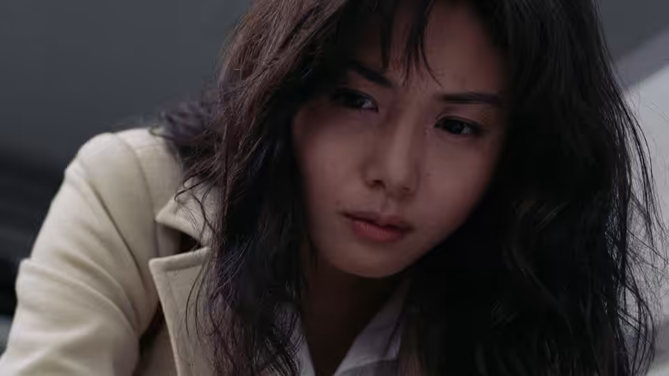 Reiko (Nanako Matsushima) leans forward in a pale coat, looking down