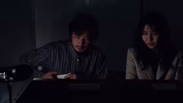 Ryuji Takayama (Hiroyuki Sanada) writing at a desk while a woman watches nearby