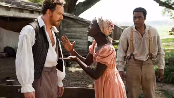 William Ford (Benedict Cumberbatch) faces Patsey (Lupita Nyong'o) gesturing toward Solomon Northup (Chiwetel Ejiofor)