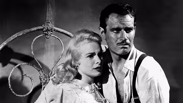 Susan Vargas (Janet Leigh) leans close to Ramon Vargas (Charlton Heston) beside an ornate metal railing