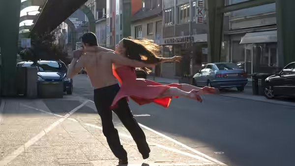 A man lifts a woman in a red dress as they dance on a city street