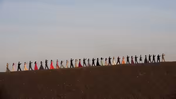 A long line of dancers walks across a barren ridge