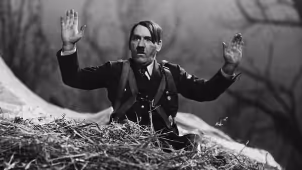 man in military uniform raises both hands while seated in straw