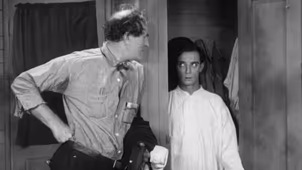 A man in work clothes turns toward another person standing inside a doorway