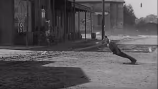 A man braces himself beside a riverside building as water rushes past