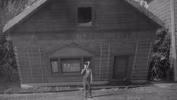 Steamboat Bill Jr. (Buster Keaton) stands before a large wooden house
