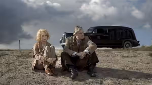 Rachel (Carice van Houten) and Müntze (Sebastian Koch) sit beside a parked car in the countryside