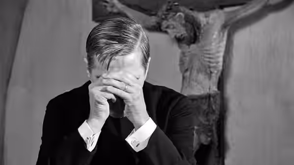 Tomas Ericsson (Gunnar Björnstrand) bows his head with clasped hands beneath the crucifix