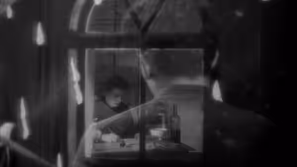 A priest writes at a desk, seen through a window from outside