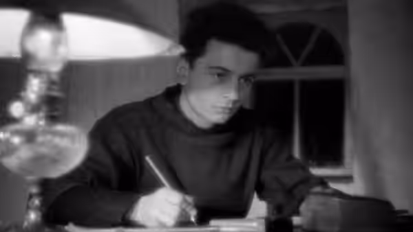 Curé d'Ambricourt (Claude Laydu) writes at a desk beside a lamp