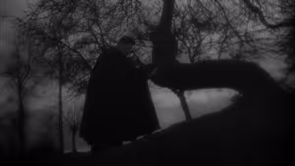 A cloaked priest walks beneath bare trees, reaching toward a branch