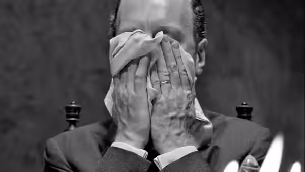 A suited man presses a cloth over his face