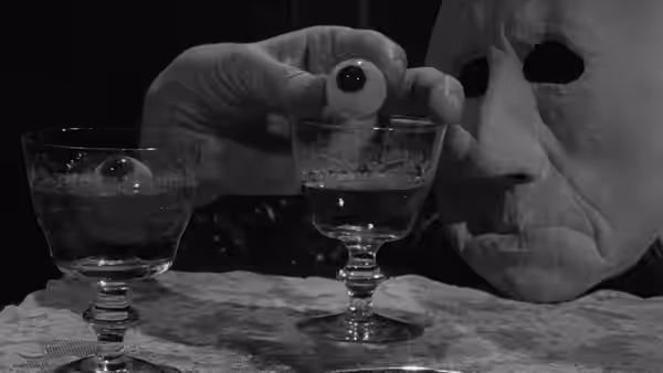 A hand holds a small round object above a glass of liquid