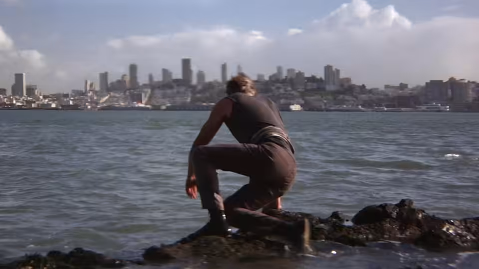 Walker (Lee Marvin) crouches on a rocky shoreline overlooking the city across the water