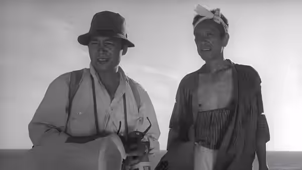 Two men in work clothes stand in the open dunes, looking ahead
