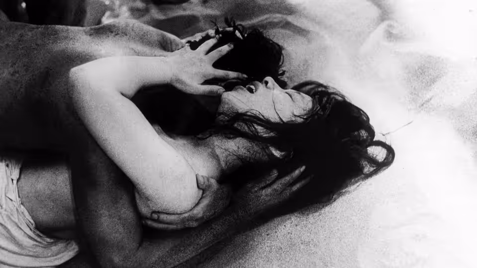 A dark-haired woman lies back as a man leans over and embraces her