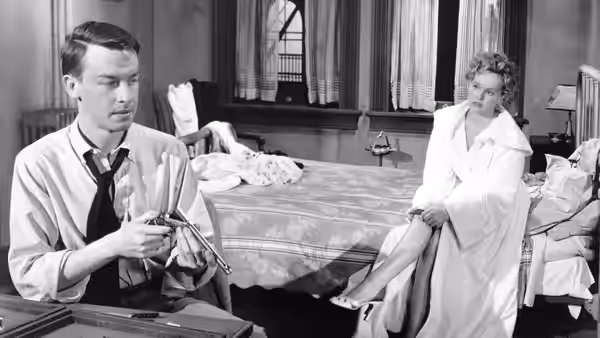 Bart Tare (John Dall) examines a revolver as Annie Laurie Starr (Peggy Cummins) sits on a bed