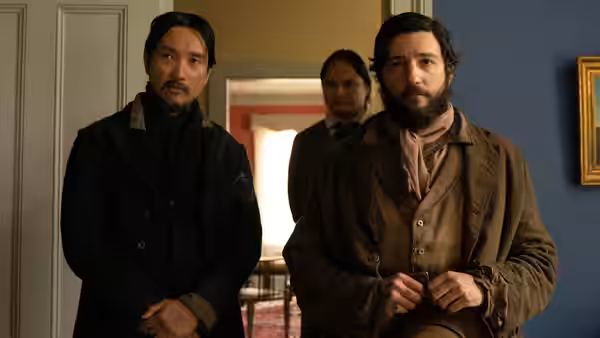 King-Lu (Orion Lee) and Cookie (John Magaro) stand in a doorway with a woman behind them