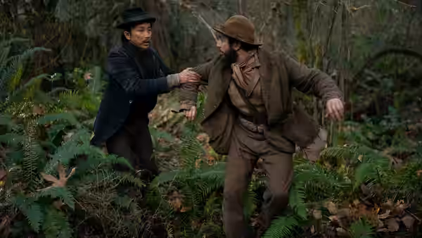 King-Lu (Orion Lee) grabs Cookie (John Magaro) as they hurry through ferns