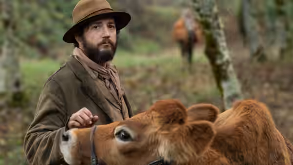 Cookie (John Magaro) rests a hand on a calf in a forest clearing