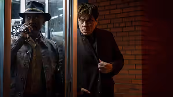 Man in hat speaking on phone beside another man at a glass door