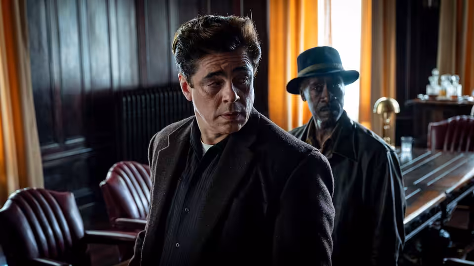 Two men in coats standing in a wood-paneled room with red leather chairs