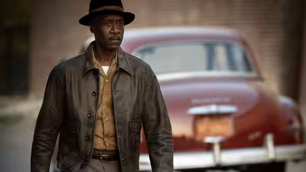 Man in leather jacket and hat standing before a vintage red car
