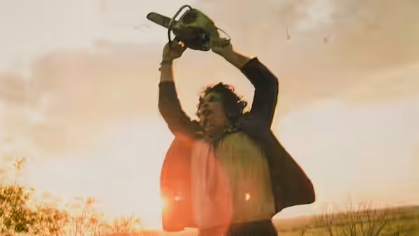 Man raising a chainsaw high overhead in a field at sunset