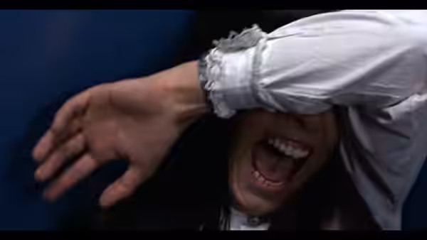 A man shields his face with his sleeve, mouth open in a scream