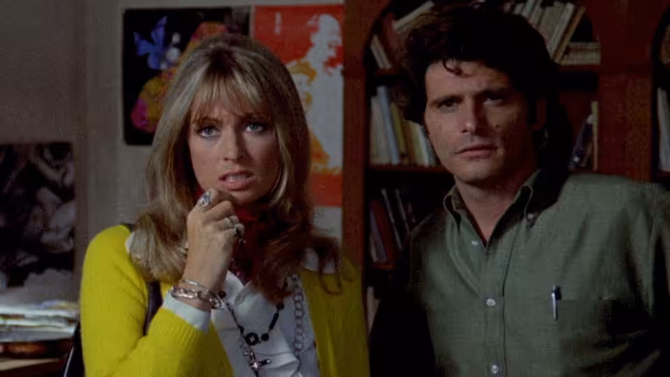 Julia (Suzy Kendall) and Sam Dalmas (Tony Musante) stand side by side indoors