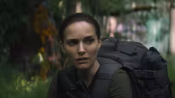 Lena (Natalie Portman) crouches alert with a large backpack in dense forest